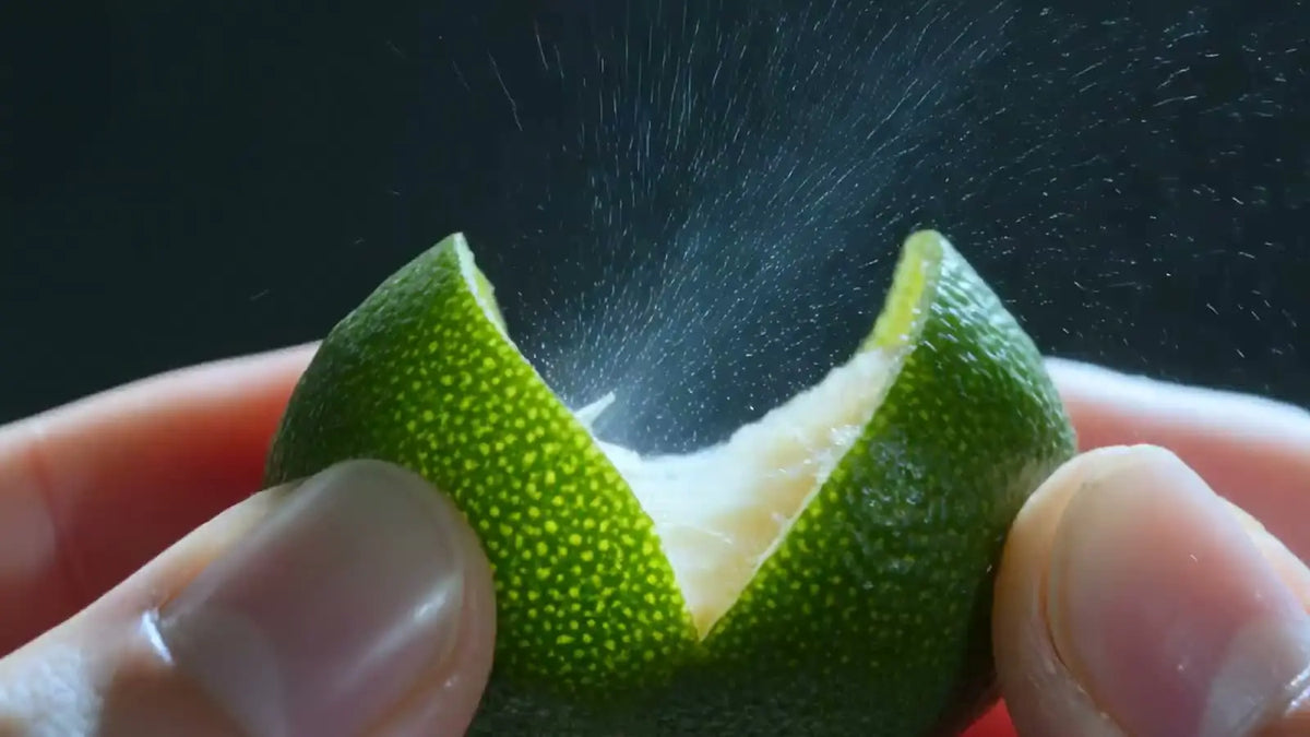 Aufgeschnittene Limette, aus deren Schale feine Öltröpfchen sprühen